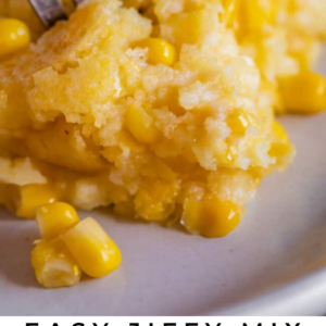 A close-up of a fork taking a bite of creamy corn casserole with whole corn kernels, featuring a moist, golden texture. Text below reads “Easy Jiffy Mix Creamed Corn Casserole - The Food Charlatan.”.