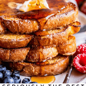 A stack of thick caramelized French toast slices topped with butter and syrup, served with fresh strawberries and blueberries. Text at bottom reads: “Seriously Amazing Caramelized French Toast. The Food Charlatan.”.