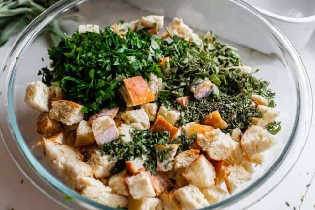 fresh chopped herbs on top of toasted bread cubes in a bowl