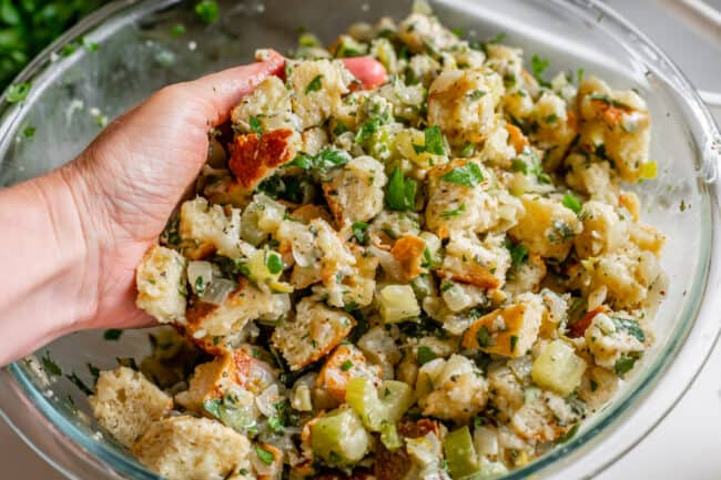 hand mixing raw stuffing together in a bowl