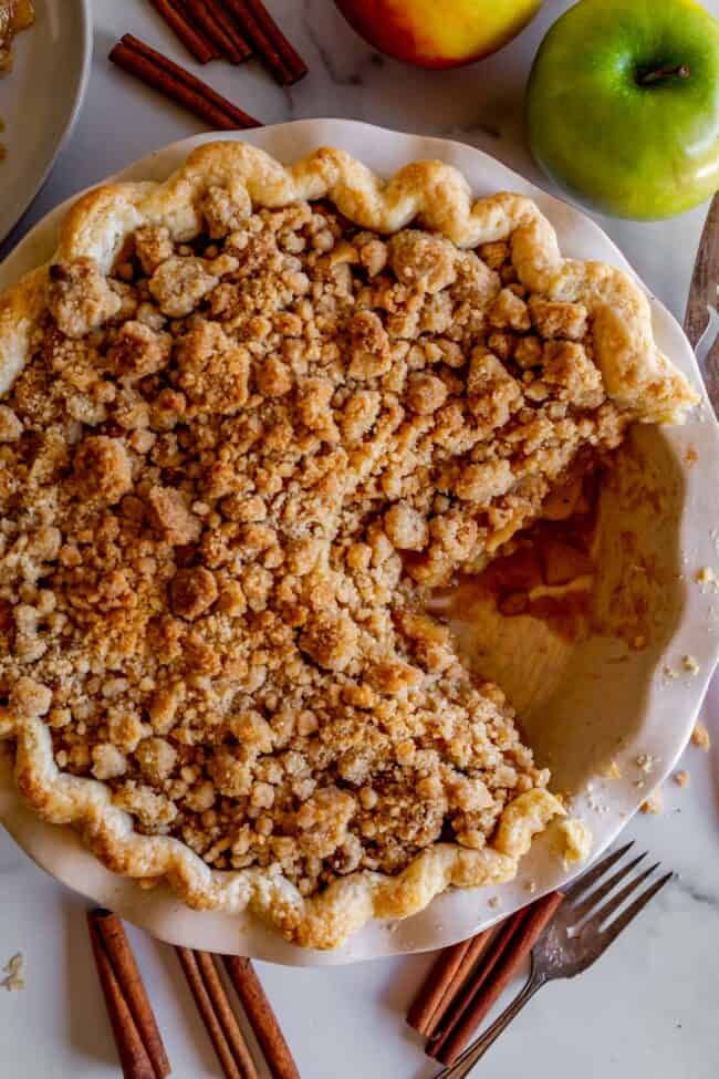 crumble top dutch apple pie in a white pie plate with a large slice cut out of it. 
