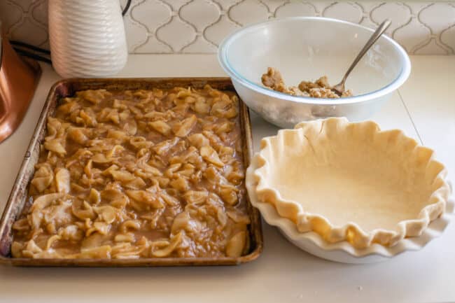apple pie filling on a sheet pan, crimped pie crust, and streusel topping in bowl.