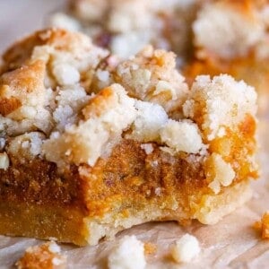 A close-up of pumpkin pie bars with a golden crust, moist filling, and buttery streusel topping, resting on brown parchment paper.