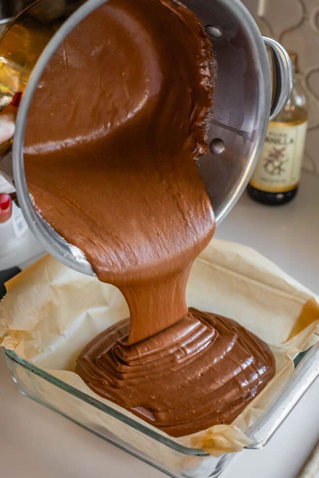 pouring fudge into parchment lined glass pan
