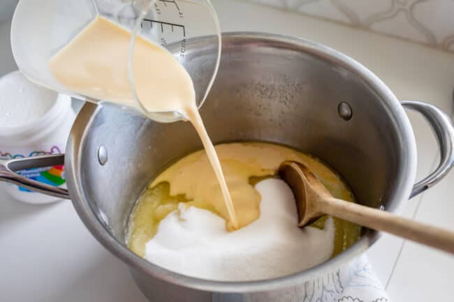 adding evaporated milk from a measuring cup to a pot of butter and sugar.