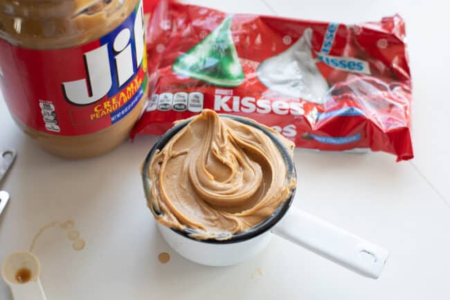 cup measurement full of creamy peanut butter, peanut butter container, and bag of Hershey's kisses.