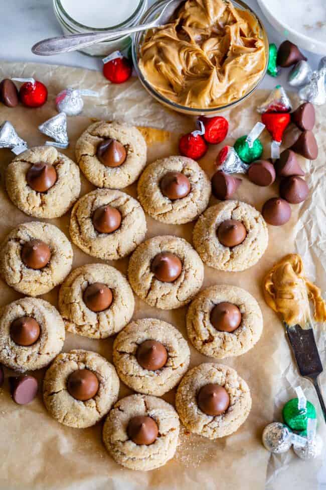 overhead shot of about a dozen peanut butter kiss cookies, a bowl of peanut butter, and Hershey's kisses.