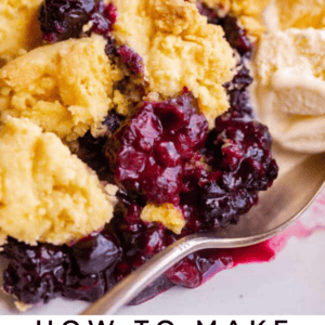 berry cobbler on a white plate with vanilla ice cream and a spoon.