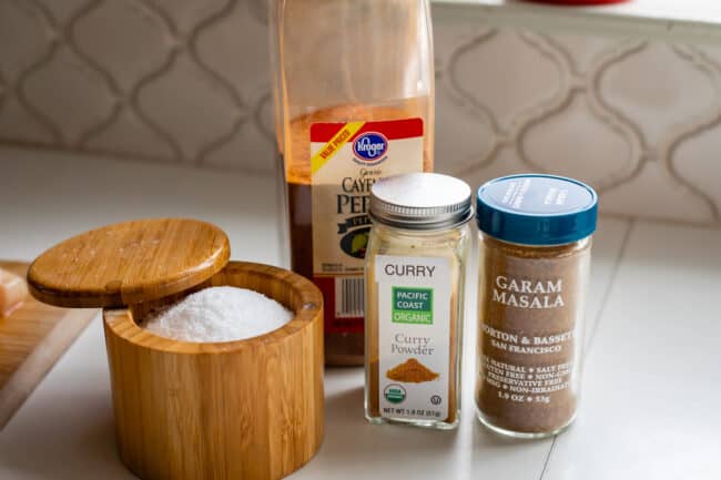 salt, cayenne, curry, and garam masala lined up in bottles on a counter