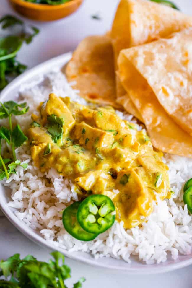 Indian curry recipe on a white plate with rice, roti, and garnishes.