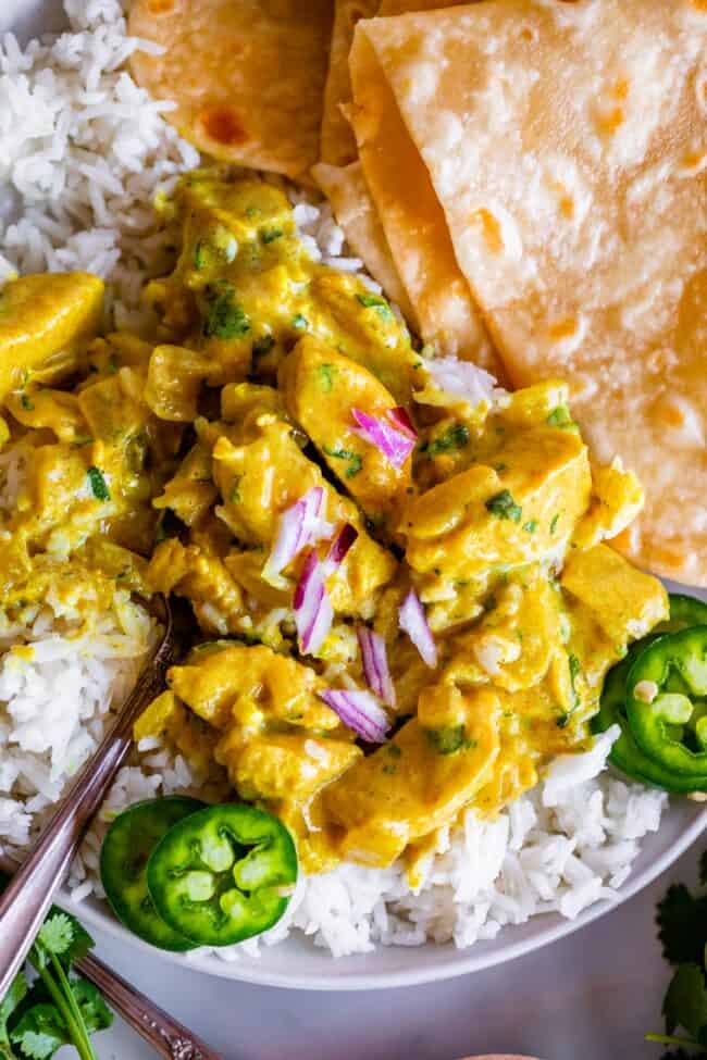 overhead shot of chicken curry on rice garnished with red onion and jalapeno.