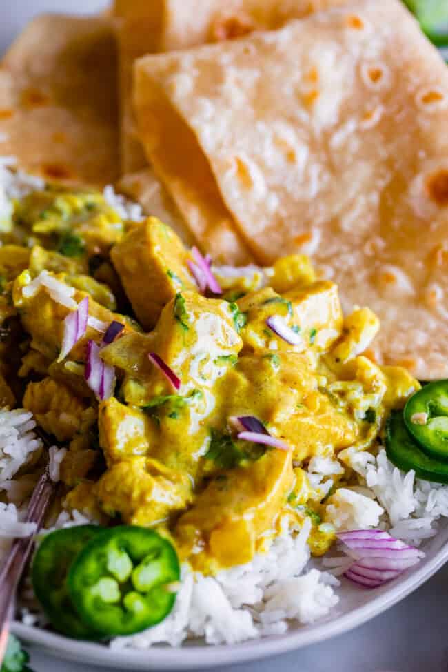 indian curry garnished with red onion and jalapeno on a plate with rice and roti.