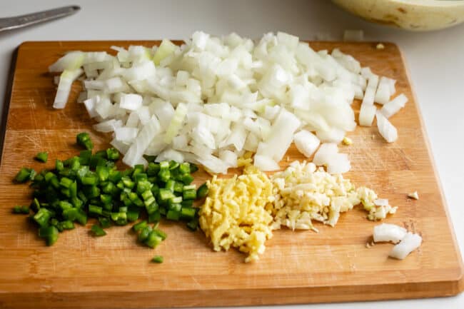 onions, jalapeno, garlic, ginger, chopped on a cutting board.