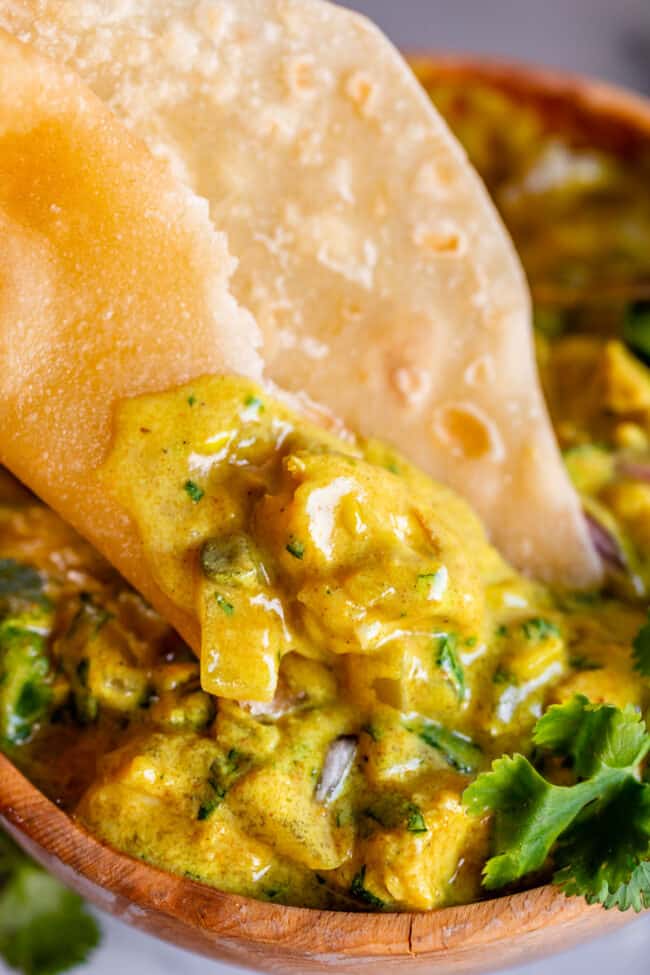 roti being dipped into a wooden bowl full of chicken curry