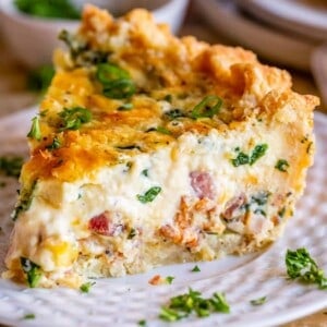 large slice of breakfast quiche on a white plate with green onions