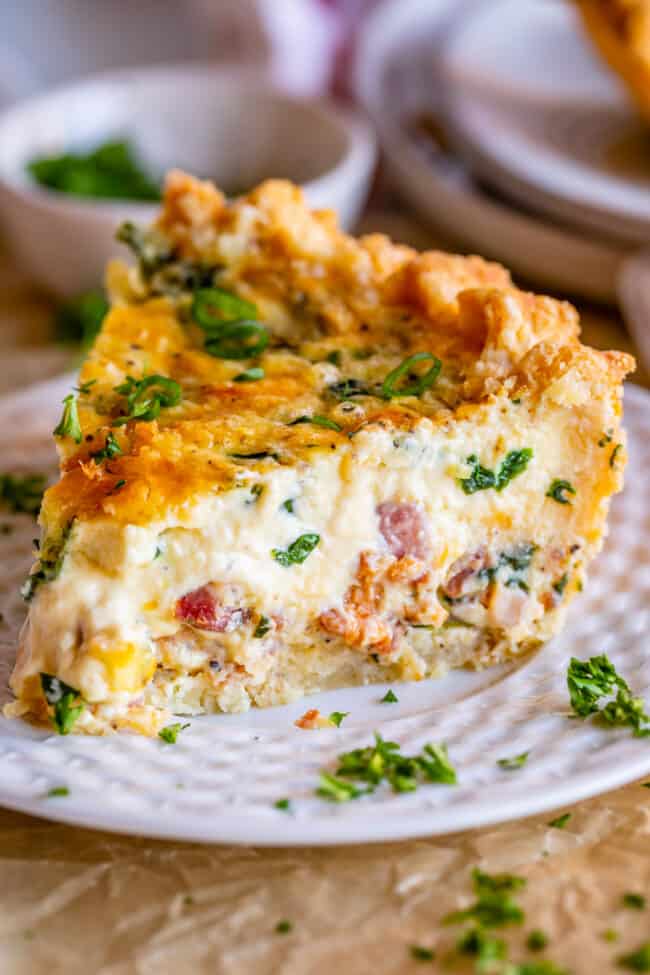 large slice of breakfast quiche on a white plate with green onions.