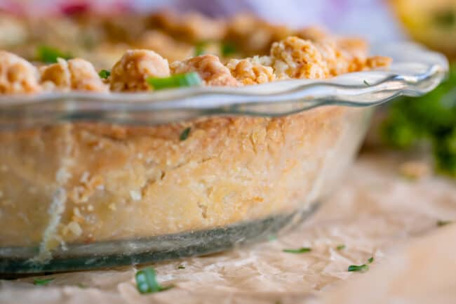 the edge of a clear glass pie pan showing the browned crust of a spinach quiche recipe.