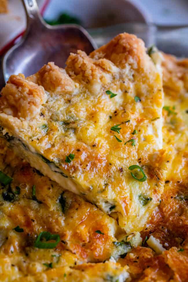 a spatula holding up a slice of basic quiche recipe with cheese and green onion.