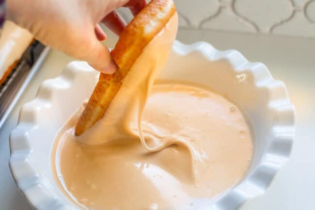 dipping bar donut into maple glaze in a pie plate