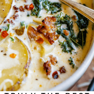 A close-up of creamy Zuppa Toscana soup with sliced potatoes, crumbled sausage, kale, and red pepper flakes in a white bowl, with a spoon submerged in the soup. Text below reads: Creamy Zuppa Toscana Soup.