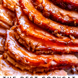 Sliced glazed ham arranged closely on a platter, garnished with a sprig of rosemary. Text at the bottom reads: Copycat Honey Baked Ham - The Food Charlatan.