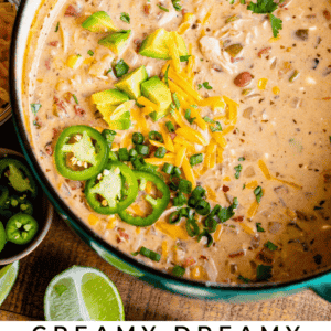 A pot of creamy white chicken chili topped with sliced jalapeños, shredded cheese, green onions, cilantro, pineapple, and lime slices sits beside fresh ingredients and lime wedges. Text: Creamy Dreamy White Chicken Chili with a burst of fresh flavor.