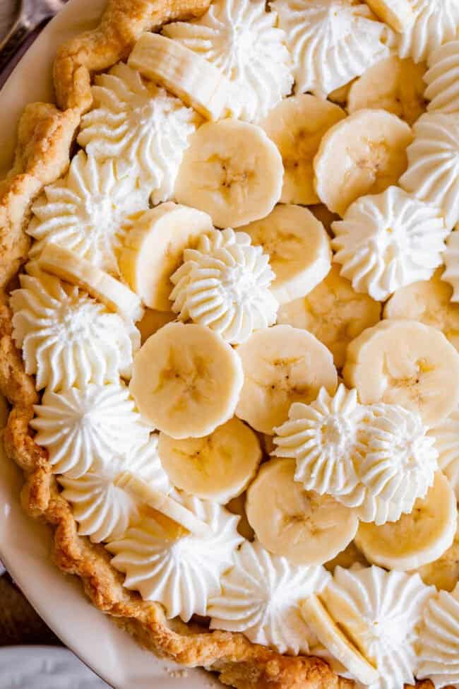 recipe for banana cream pie with banana slices on top, piped whipped cream.