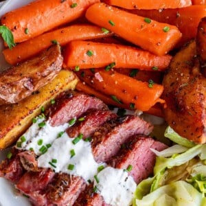 slow cooker corned beef and cabbage on a plate with horseradish sauce and carrots