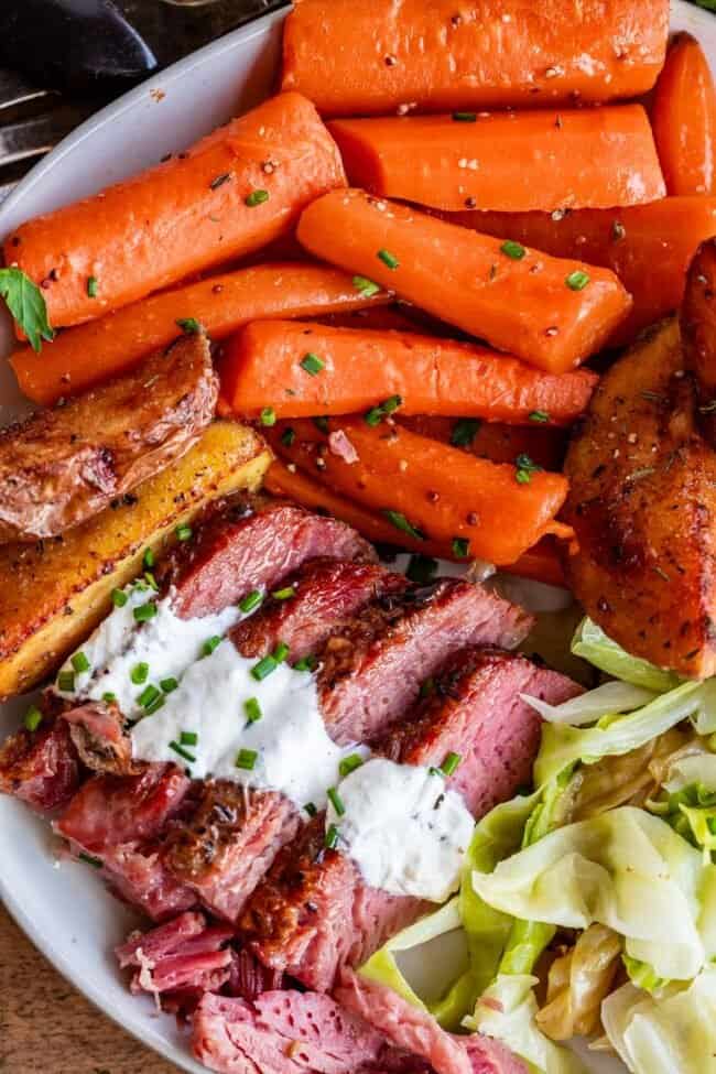 slow cooker corned beef and cabbage on a plate with horseradish sauce and carrots.