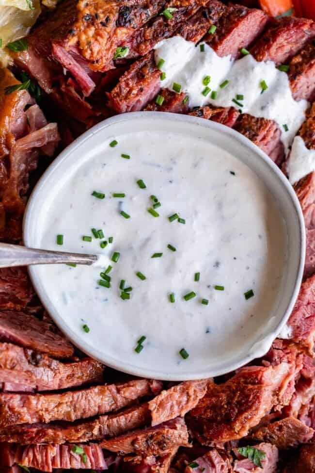 white bowl full of creamy horseradish sauce surrounded by corned beef.