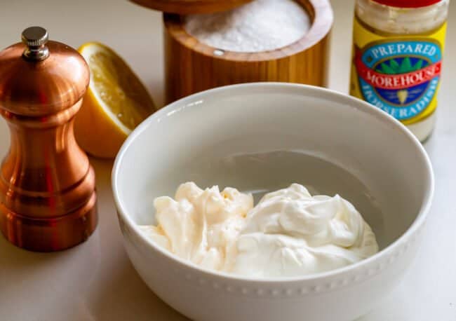 sour cream and mayo in a bowl, surrounded by pepper, lemon, salt, horseradish.
