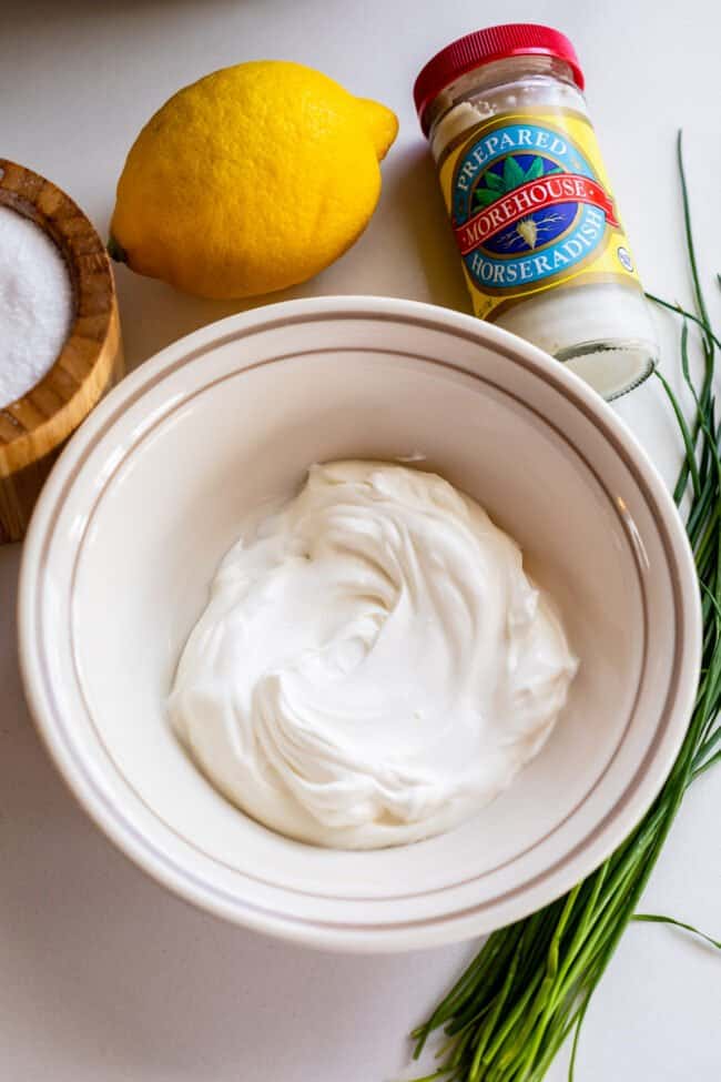 sour cream in a bowl with chives, lemon, salt, and jar of horseradish.
