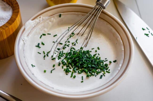 adding chopped chives to a bowl of horseradish sauce.