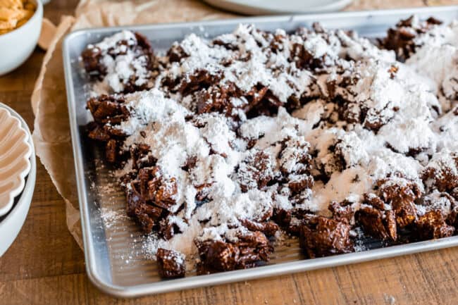 adding powdered sugar to chocolate covered Chex on a baking sheet.