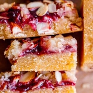 raspberry almond bars stacked up on parchment paper.