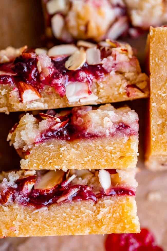 raspberry almond bars stacked up on parchment paper.