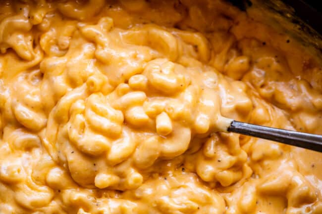 Spoon lifting a bite of mac and cheese from a slow cooker