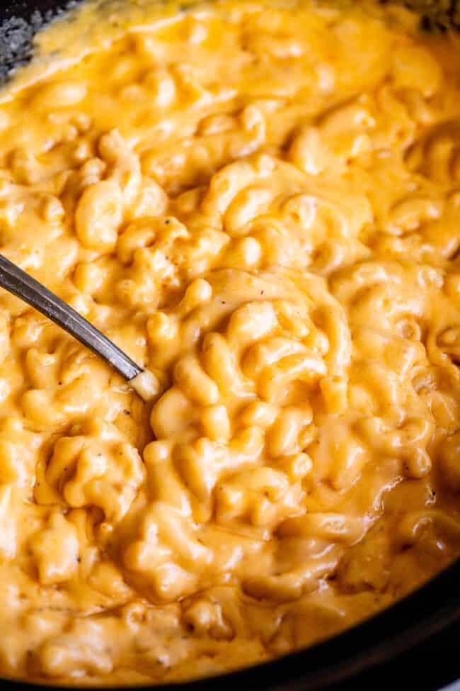 slow cook mac and cheese in a black crock pot with spoon for serving.