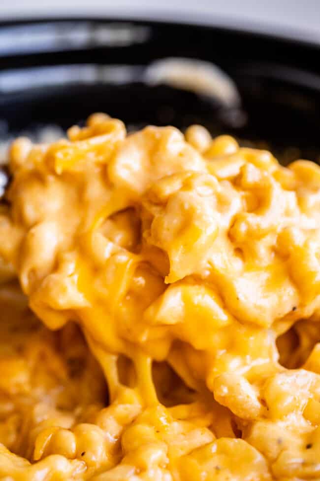 mac and cheese in slow cooker being lifted with a serving spoon, cheese pull.