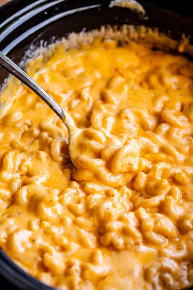 serving spoon lifting mac and cheese from a black crockpot.