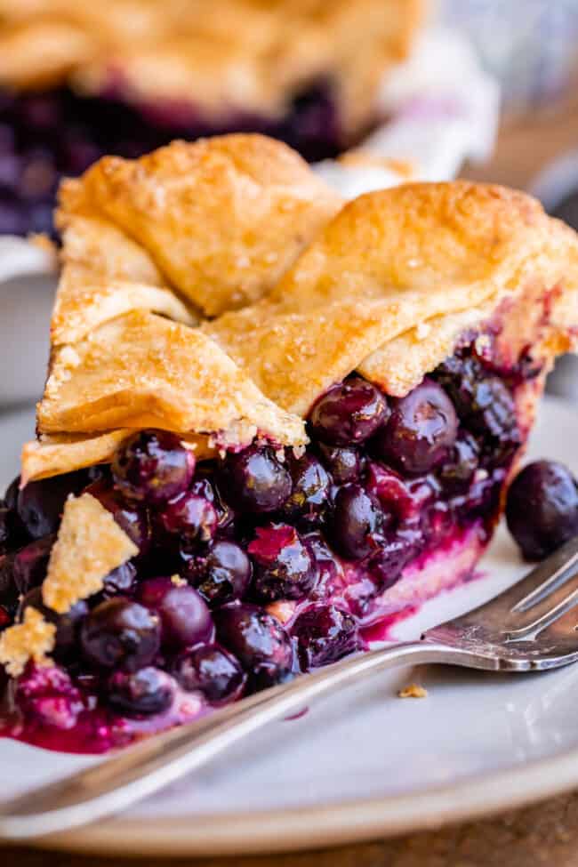 slice of blueberry pie on a plate with cream cheese layer, on white plate with fork.