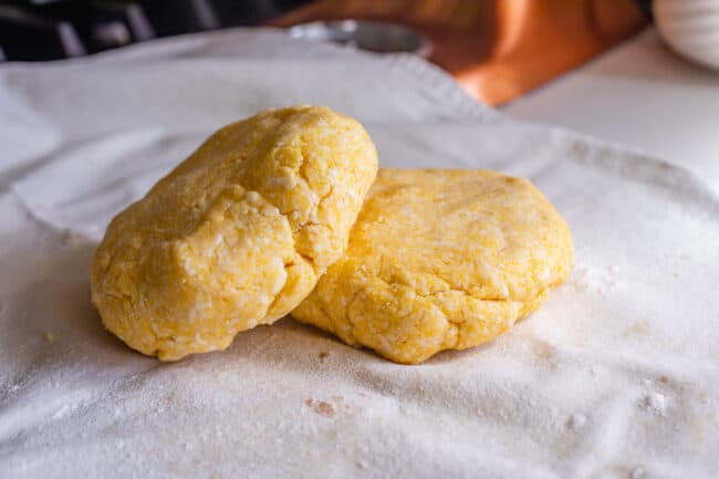 two discs of cornmeal pie dough on a pastry cloth.