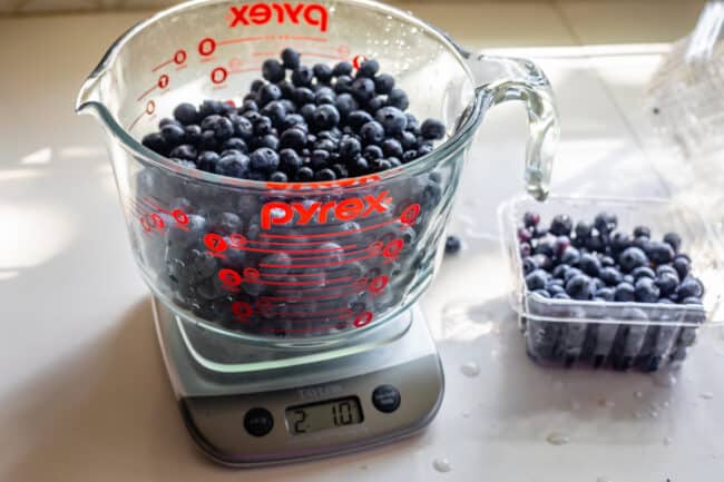 blueberries in a large glass measuring cup, on a scale weighing 2 pounds.