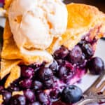 blueberry pie on a plate topped with ice cream, next to a fork.