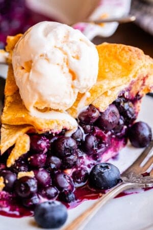 blueberry pie on a plate topped with ice cream, next to a fork.