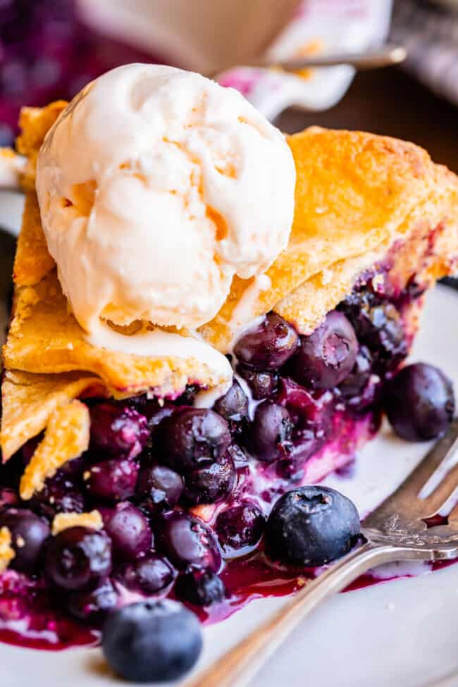 blueberry pie on a plate topped with ice cream, next to a fork.