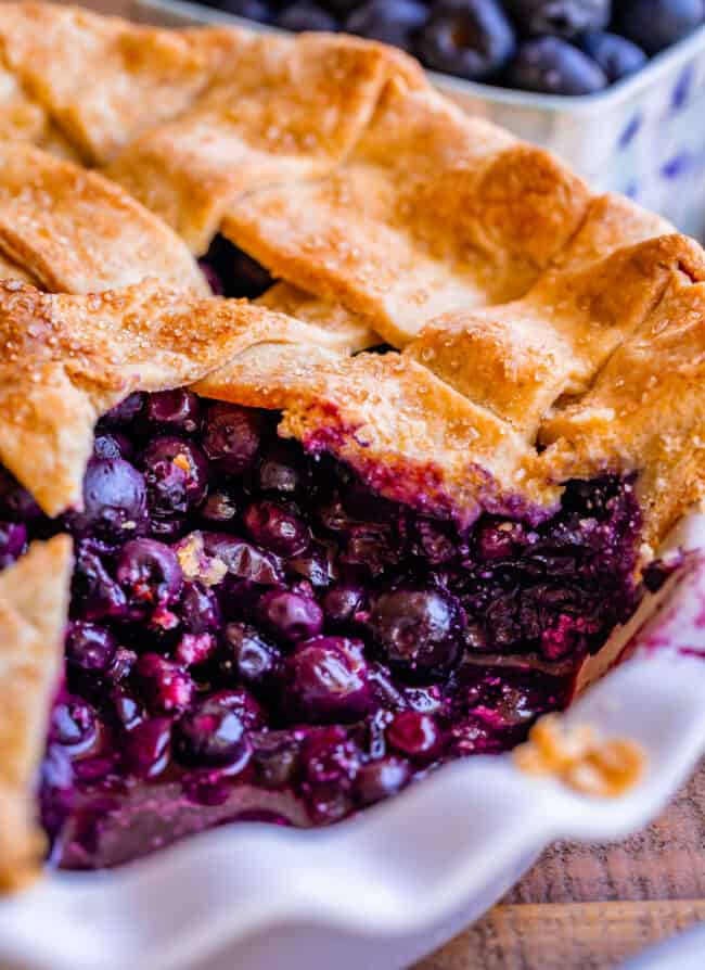 whole blueberry pie in pan with a slice missing, berries in the middle.