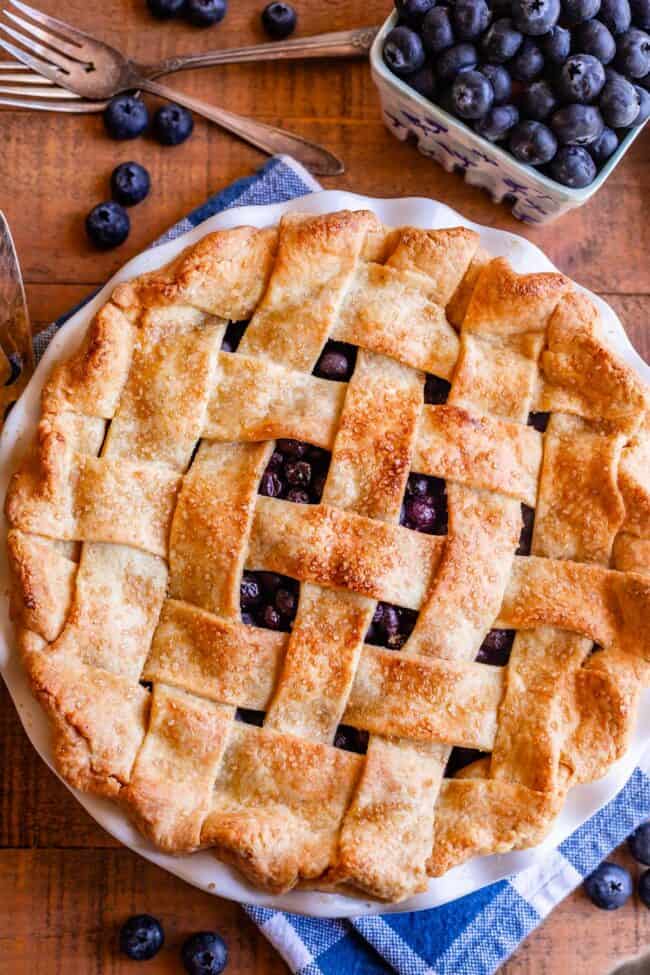 baked best blueberry pie recipe with a lattice crust, shot from overhead with a bowl of blueberries on the side.
