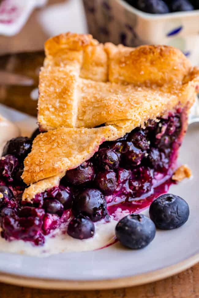 the best blueberry pie recipe with a flaky crust, on a white plate with melted ice cream.