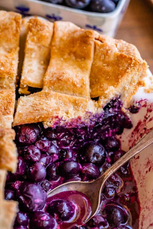 best blueberry pie recipe, sliced in a pie pan with spoon dipping into berries.